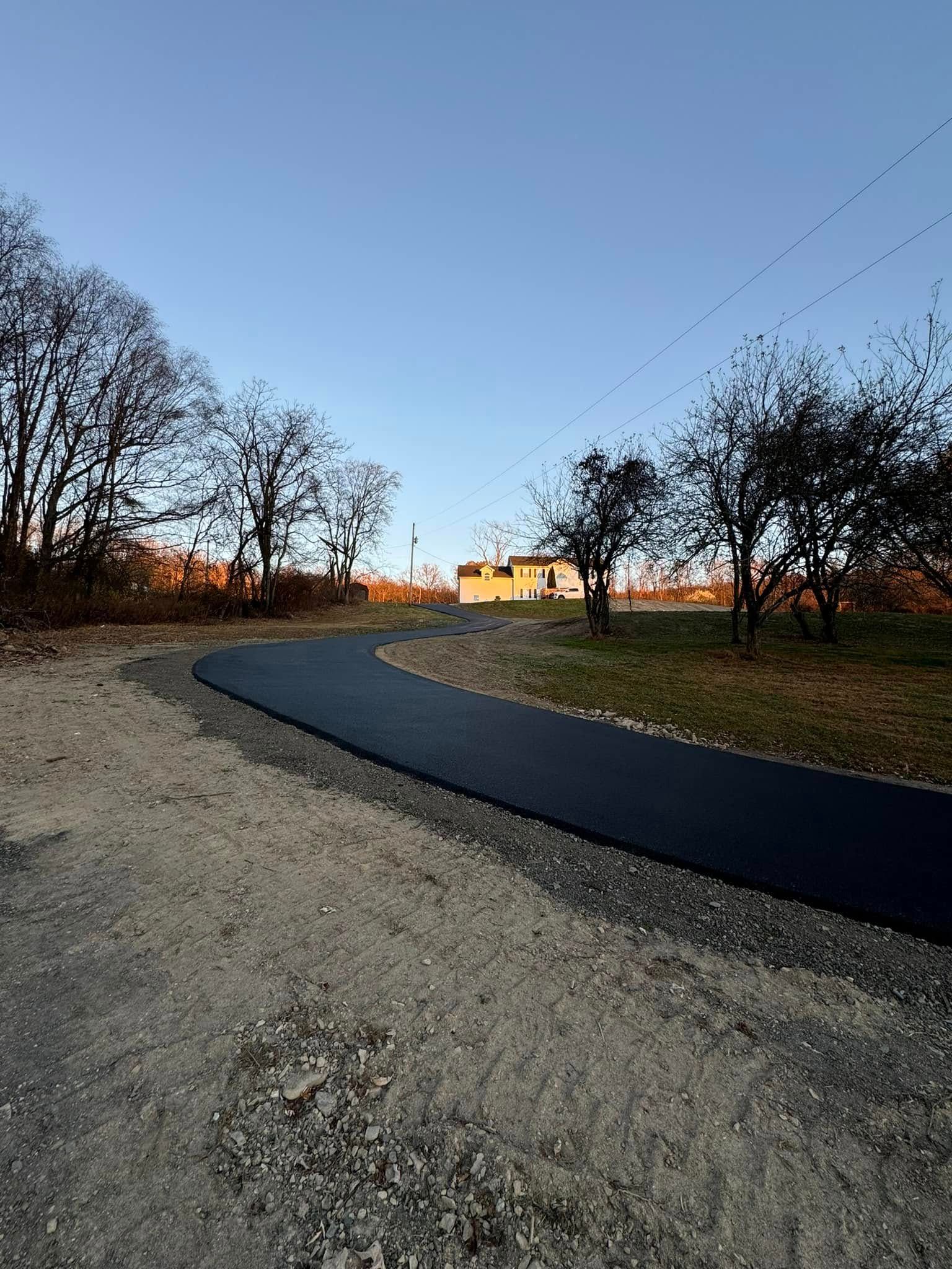 A paved, curving path winds through a grassy field towards a small building at sunset under a clear blue sky.