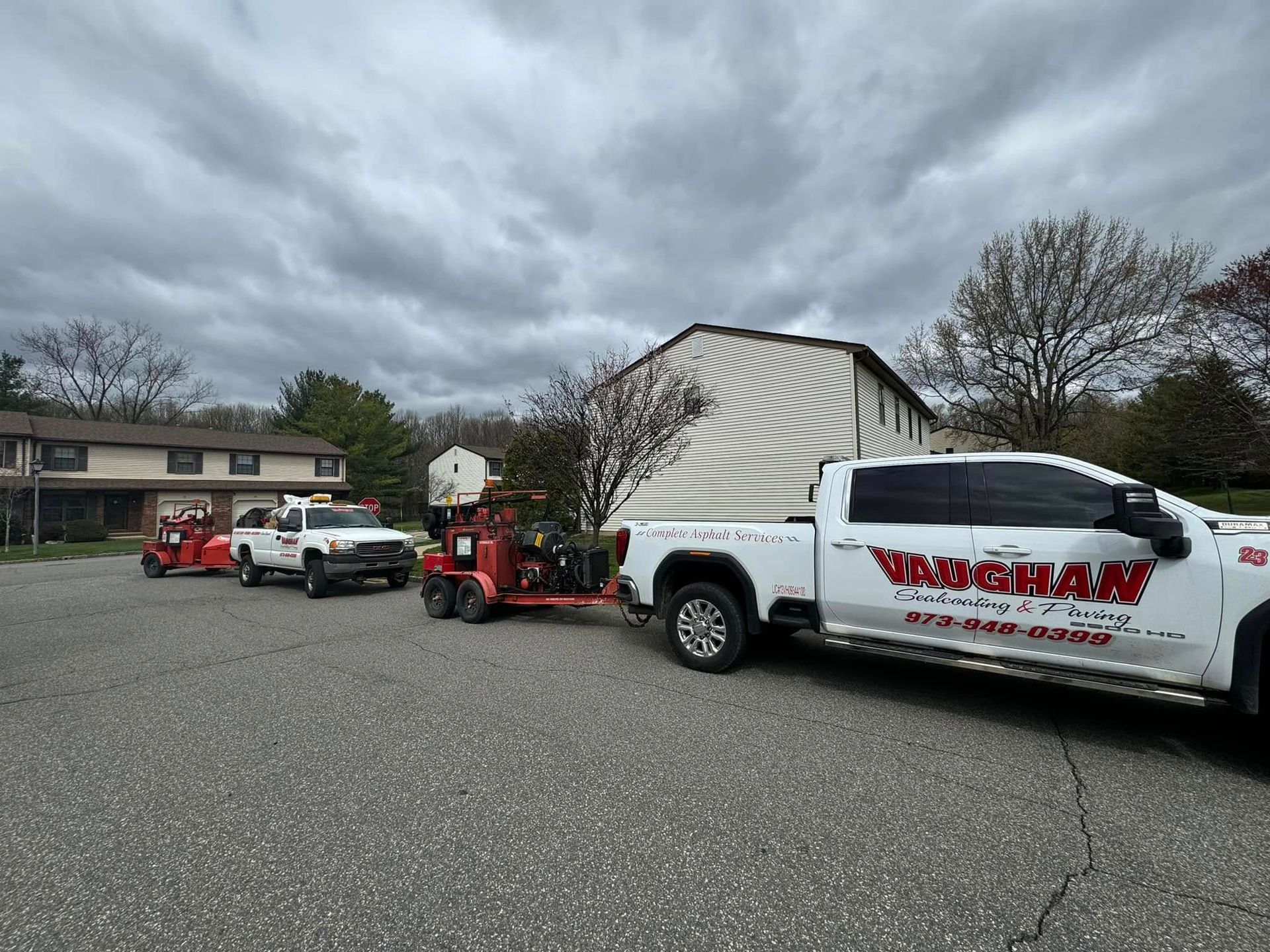 A white pickup truck with company branding on the door, pulling a trailer with machinery, parked on a gravel lot.