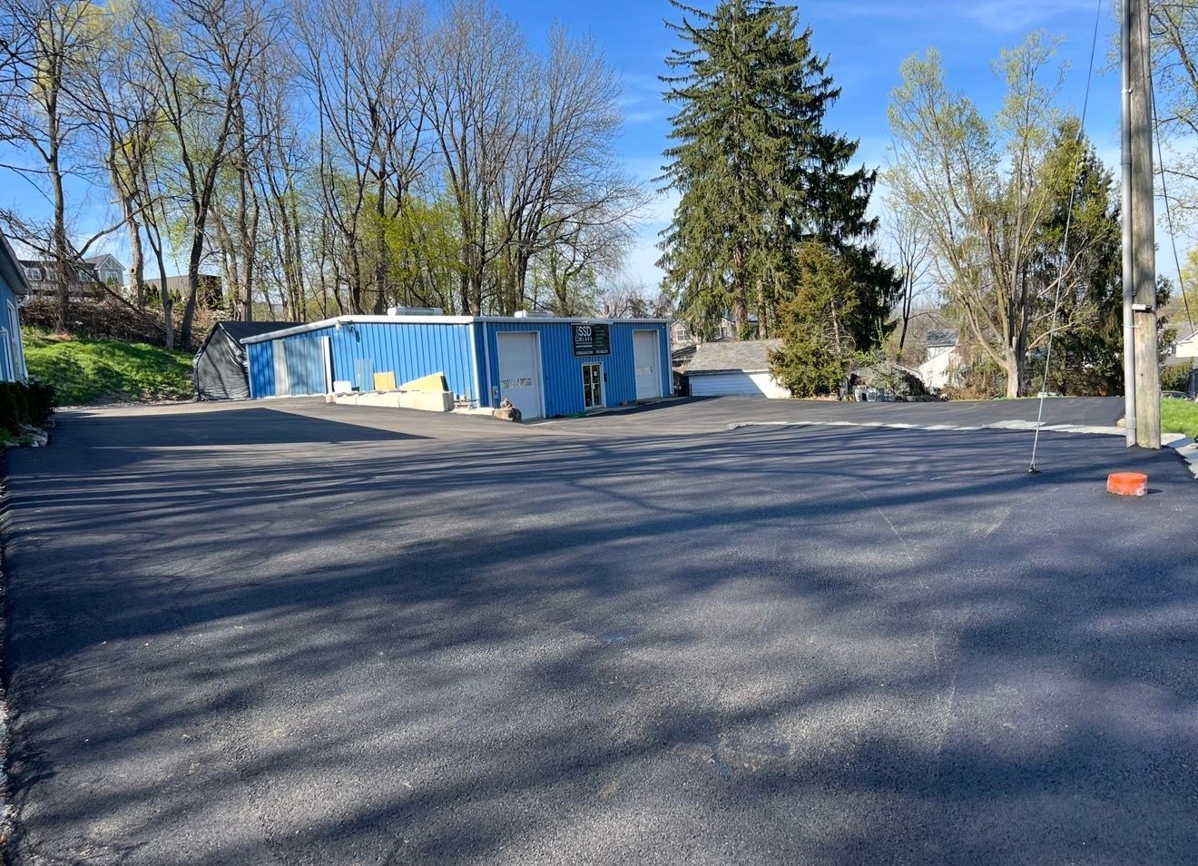 A freshly paved black asphalt parking lot in front of a blue industrial building under a clear blue sky.