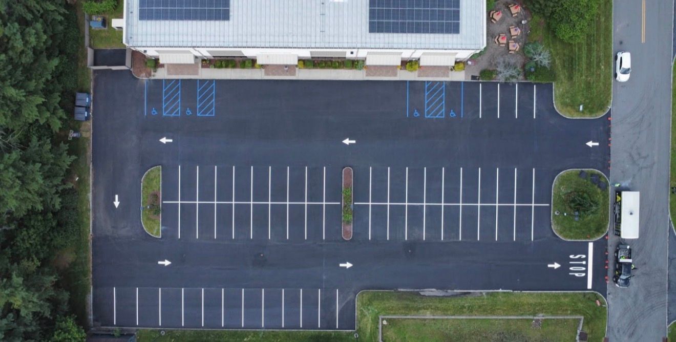 Aerial view of an empty commercial parking lot with asphalt pavement, marked parking spaces, and white directional arrows.
