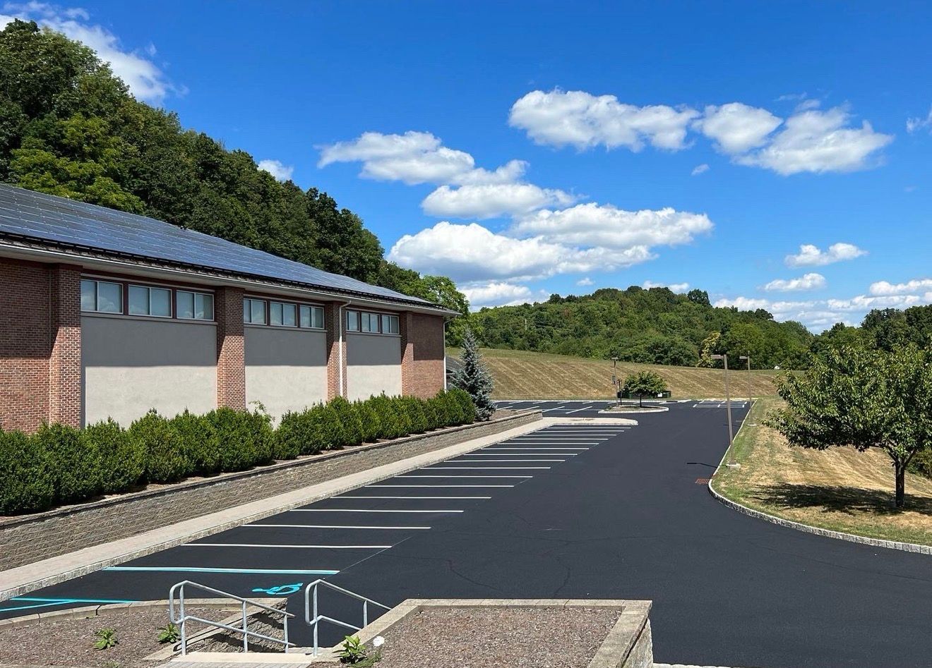 A parking lot with freshly paved asphalt and painted white spaces beside a brick building under a sunny blue sky.