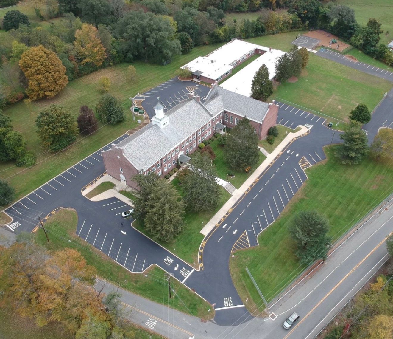 Aerial view of a brick building with a white cupola, surrounded by paved parking lots, trees, and a road.
