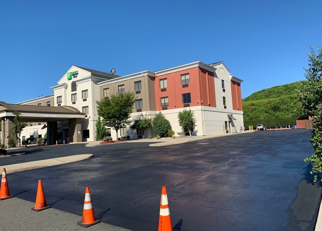 A Holiday Inn Express hotel building with a newly paved asphalt parking lot and several traffic cones.