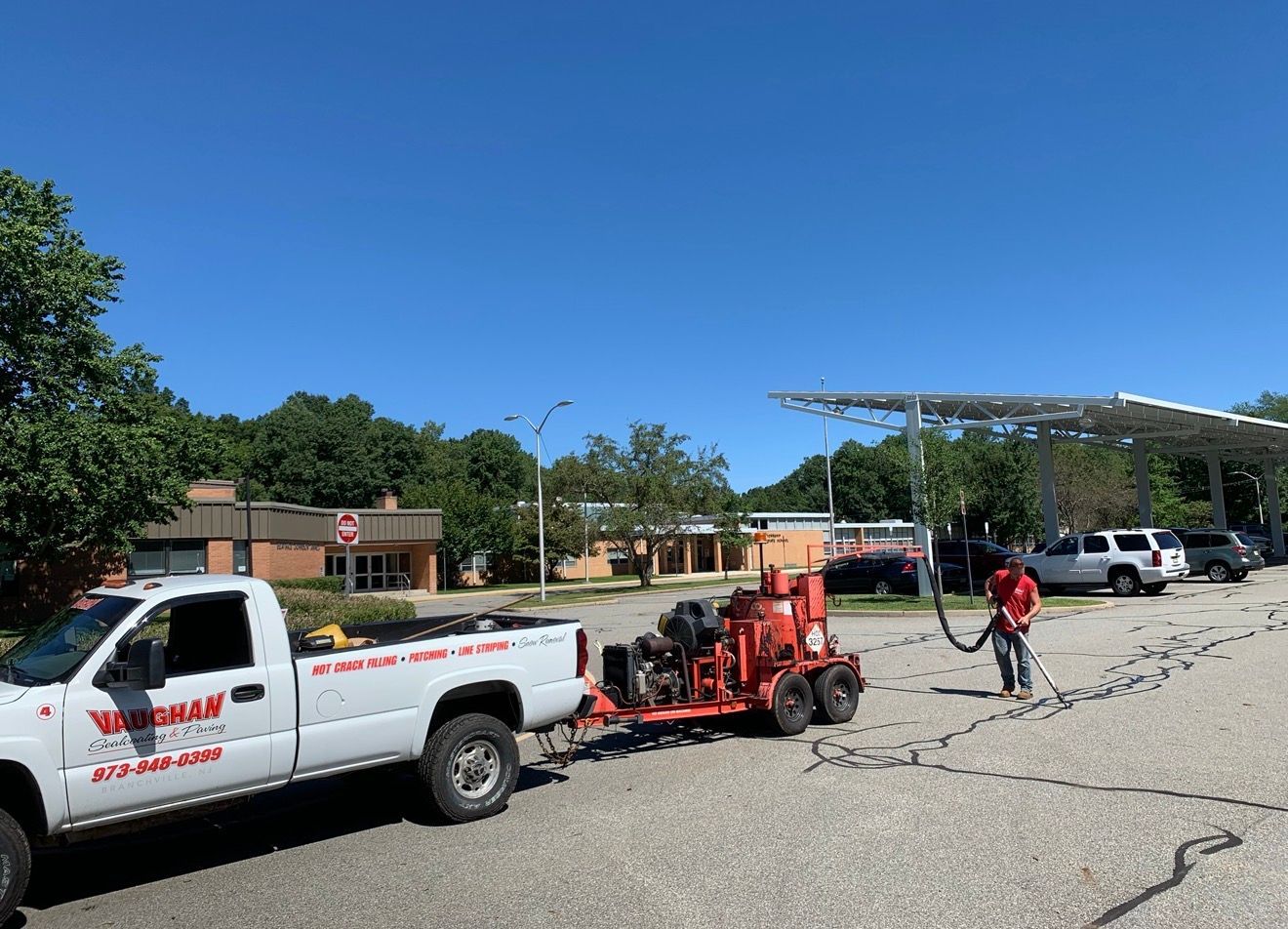 A white utility truck towing a red industrial pump machine in a parking lot, with a worker operating a hose nearby.
