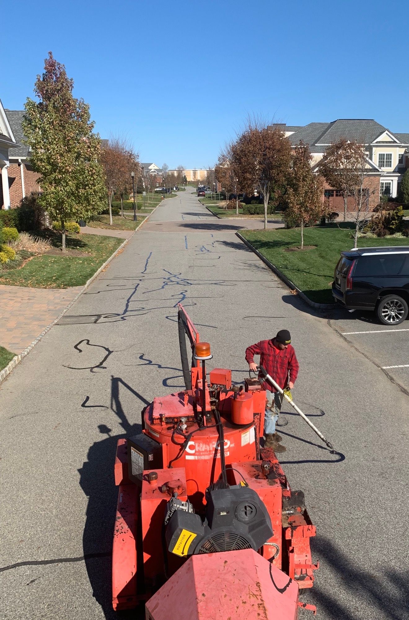 A worker operating a red asphalt crack sealing machine on a paved residential street.
