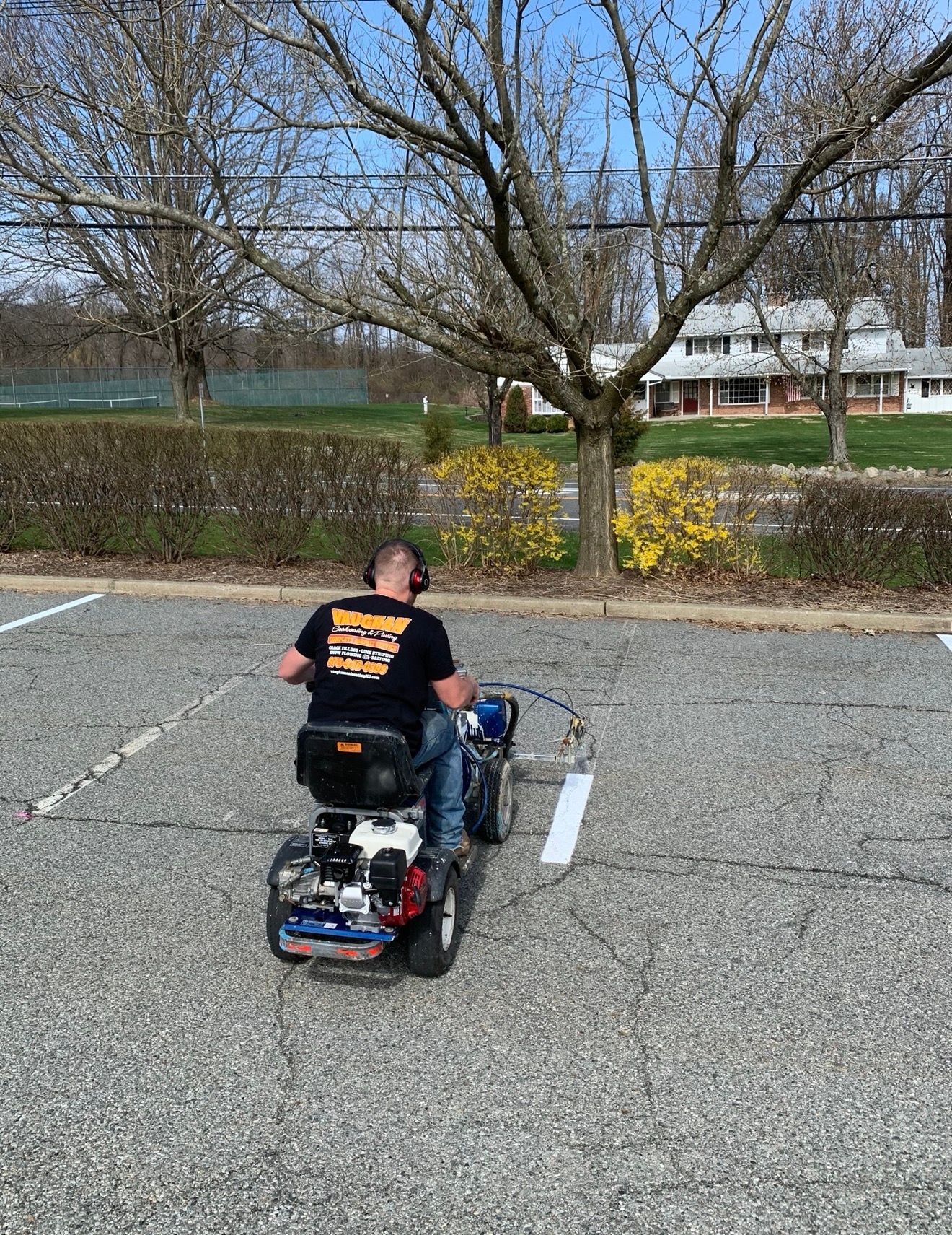 A person uses a ride-on parking lot striper machine to paint white lines on a gravel parking area.