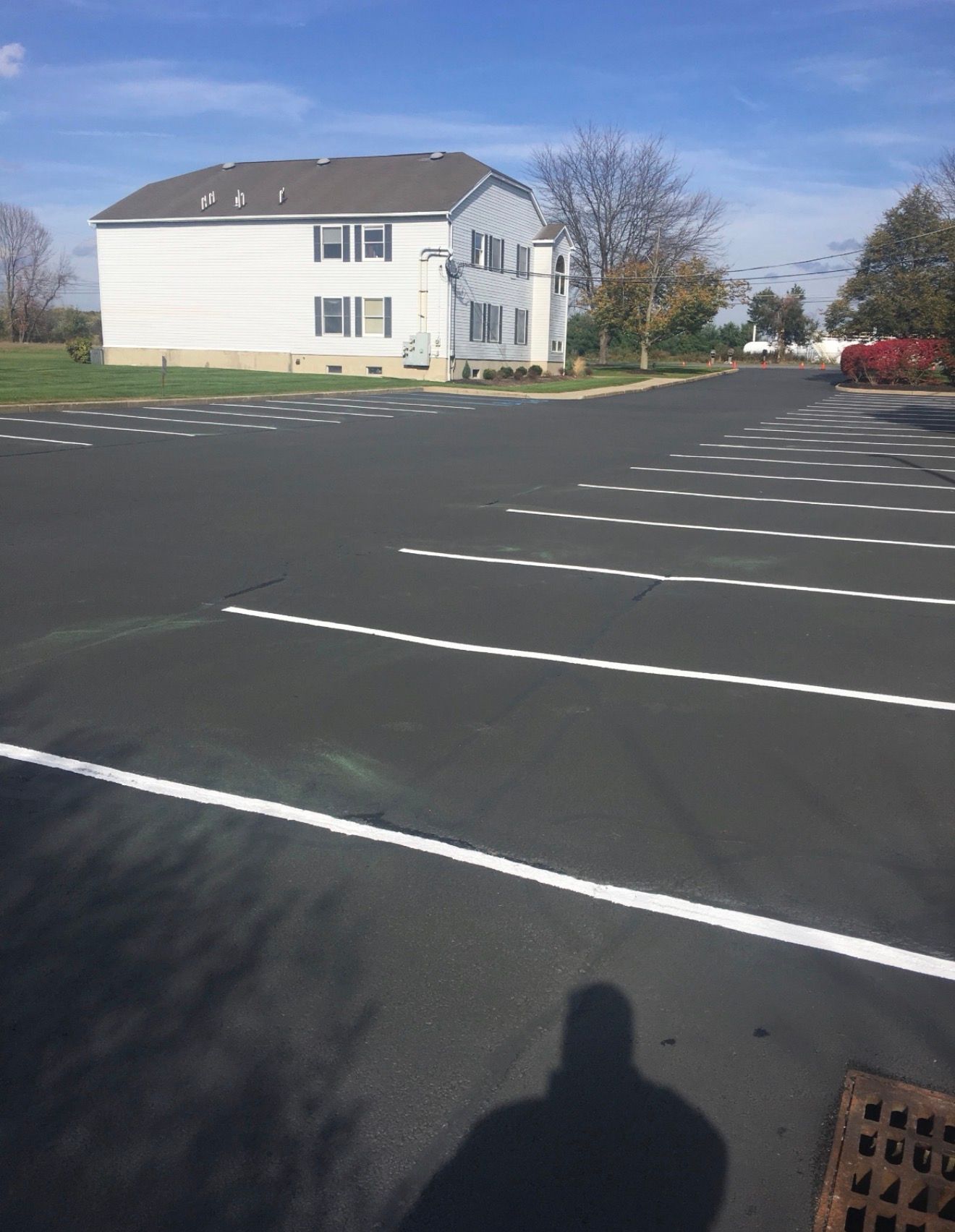 An empty parking lot with dashed white lines painted on black asphalt next to a two-story residential apartment building.
