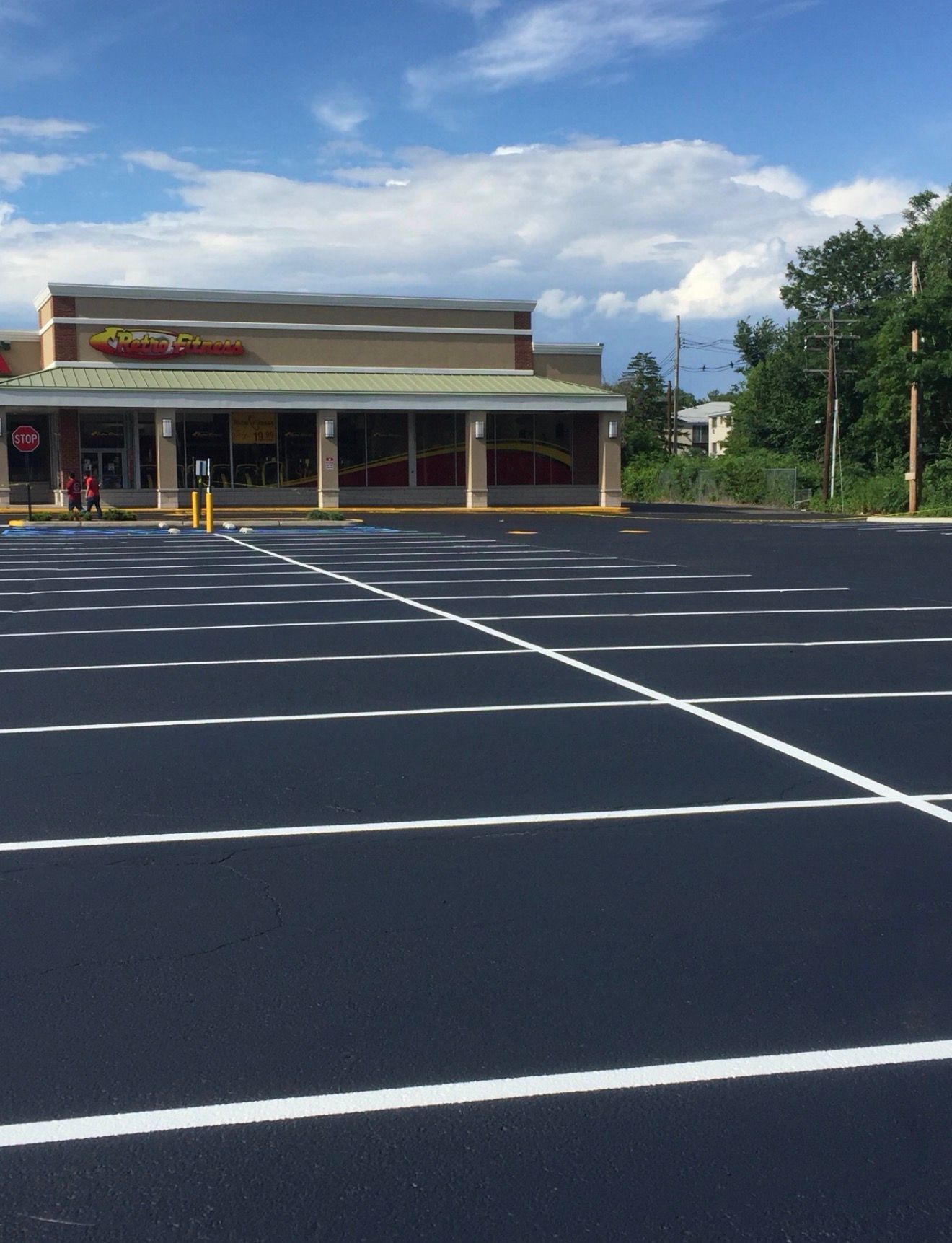 A freshly paved, empty parking lot with bright white painted lines leading toward a commercial building under a blue sky.