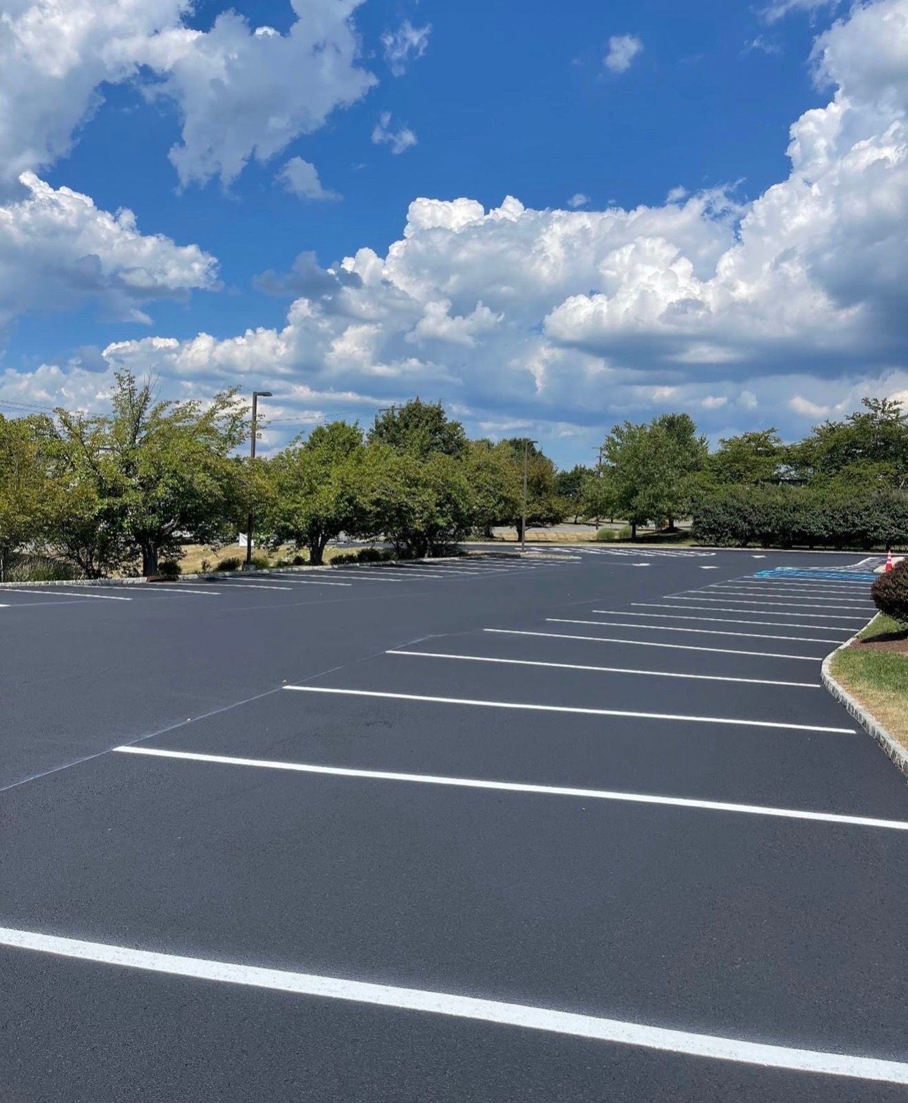 A freshly paved asphalt parking lot with newly painted white parking stall lines under a bright, partly cloudy sky.