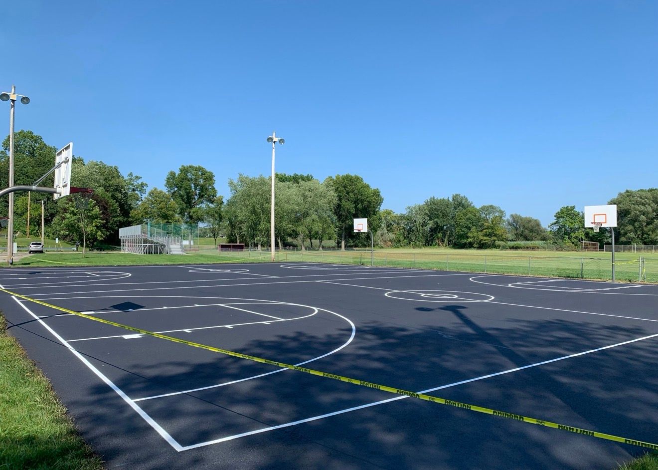 An outdoor basketball court with a freshly paved black surface and white painted boundary lines on a sunny day.