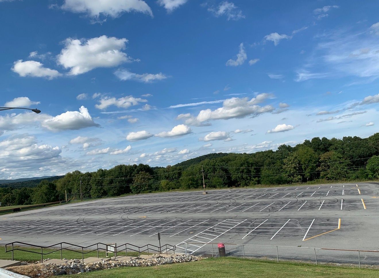 An empty, paved parking lot with painted white lines on a sunny day with blue skies and scattered clouds.