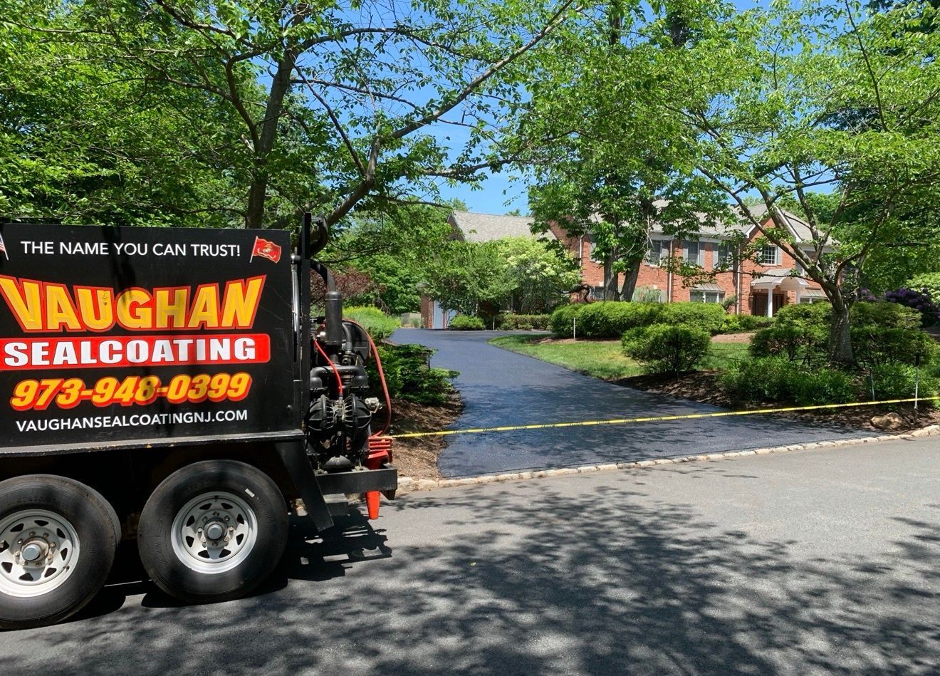 A Vaughan Sealcoating trailer parked near a freshly sealcoated driveway in front of a house on a sunny day.