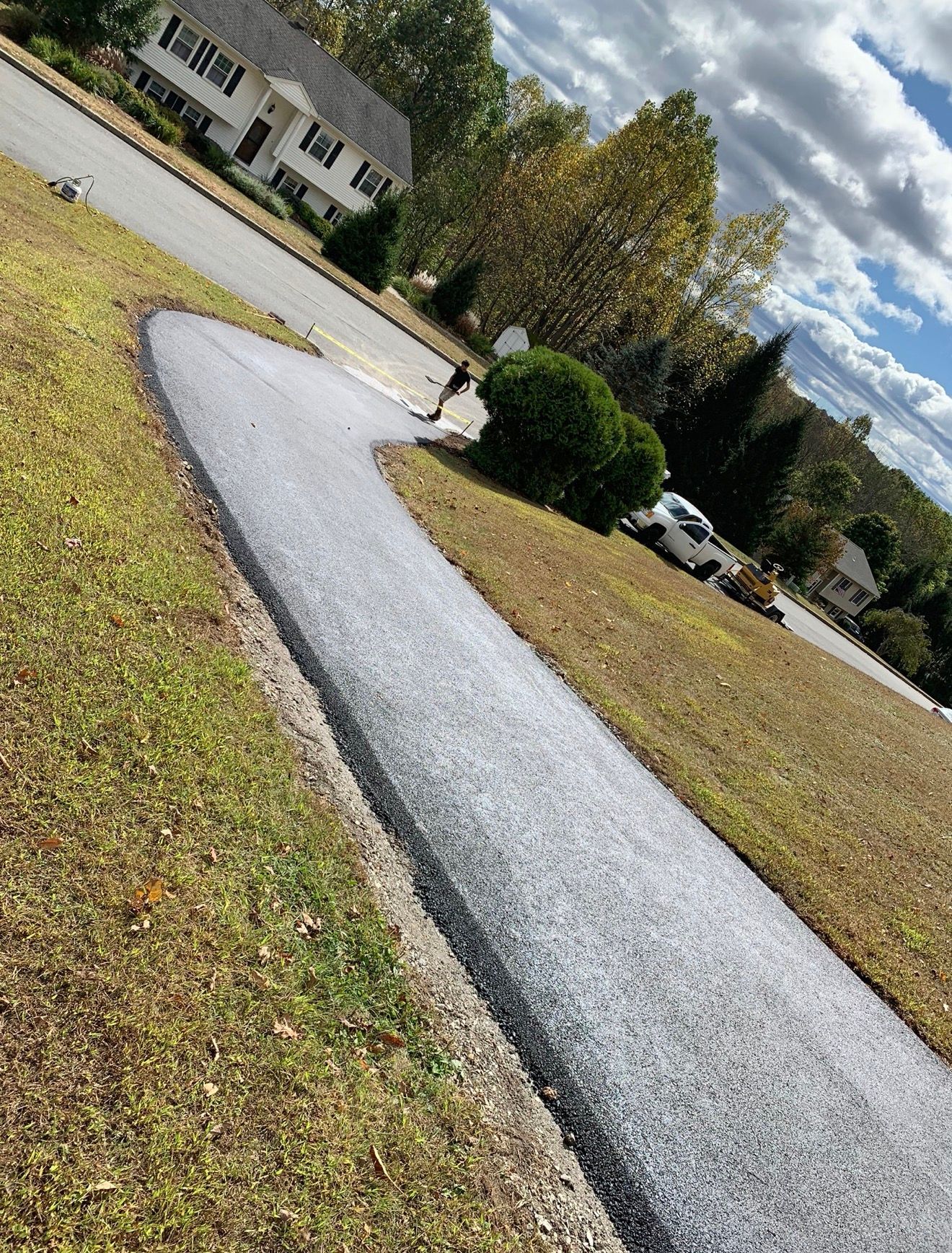 A freshly paved, light gray gravel walkway curves through a lawn toward a residential house on a sunny day.