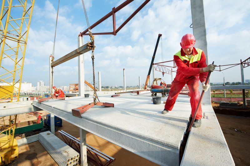 A construction worker is standing on top of a building under construction.