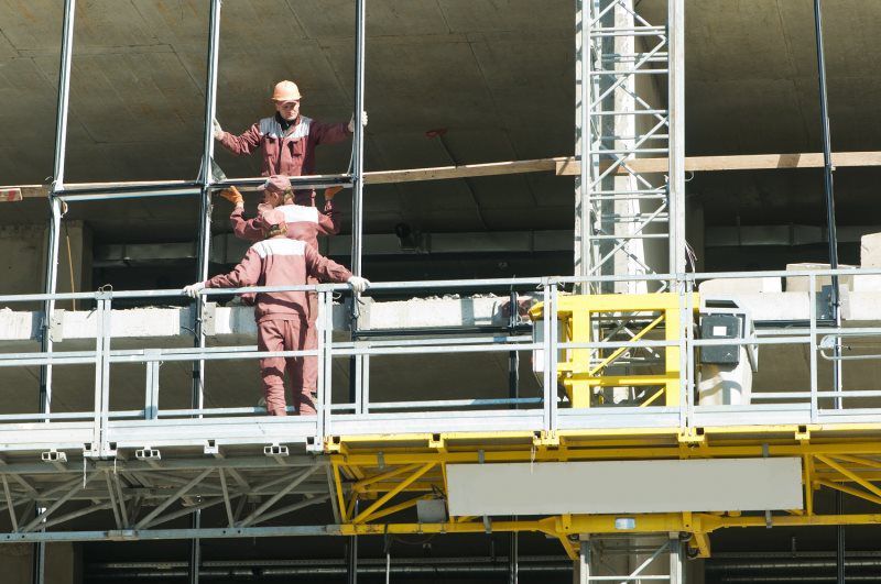 Two construction workers are standing on a scaffolding on top of a building.