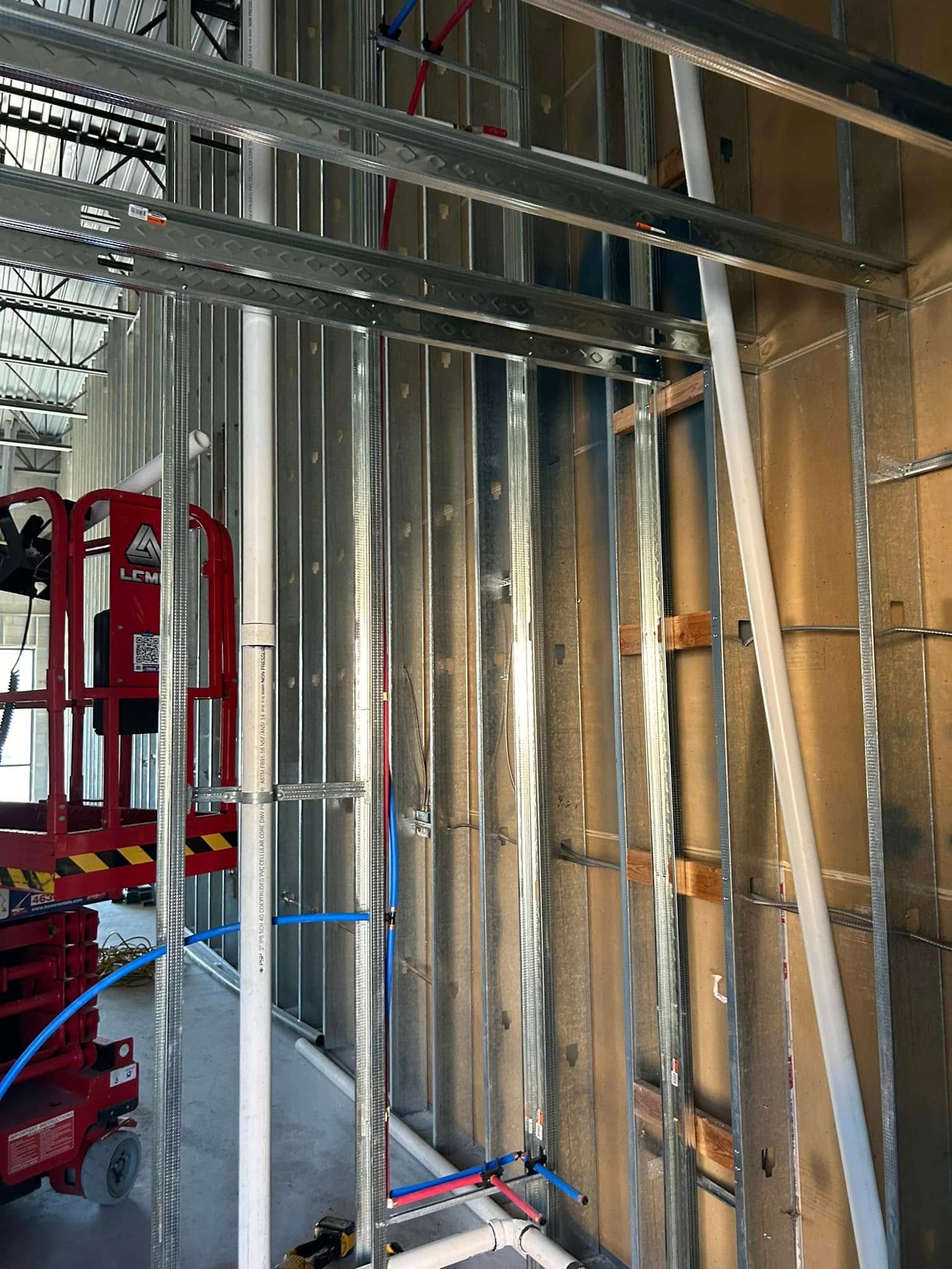 Metal framing and plumbing installed inside a new building. A lift is partially visible.