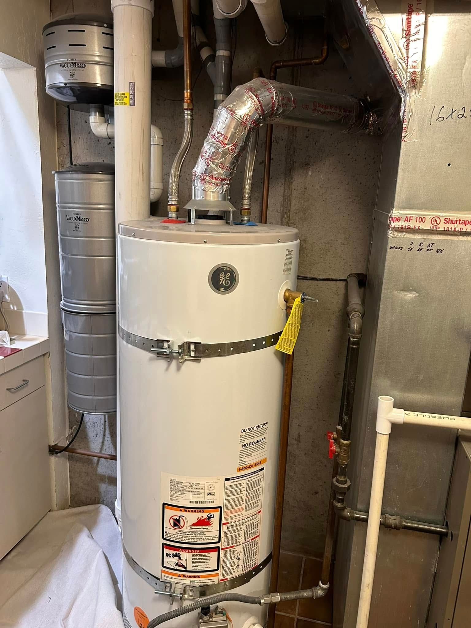 A water heater in a basement next to a stack of metal storage tanks and ductwork.