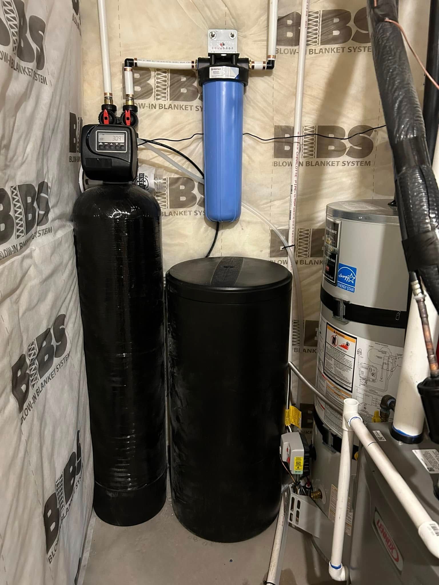 Water filtration system in a utility room. Black tanks, blue filter, white pipes.