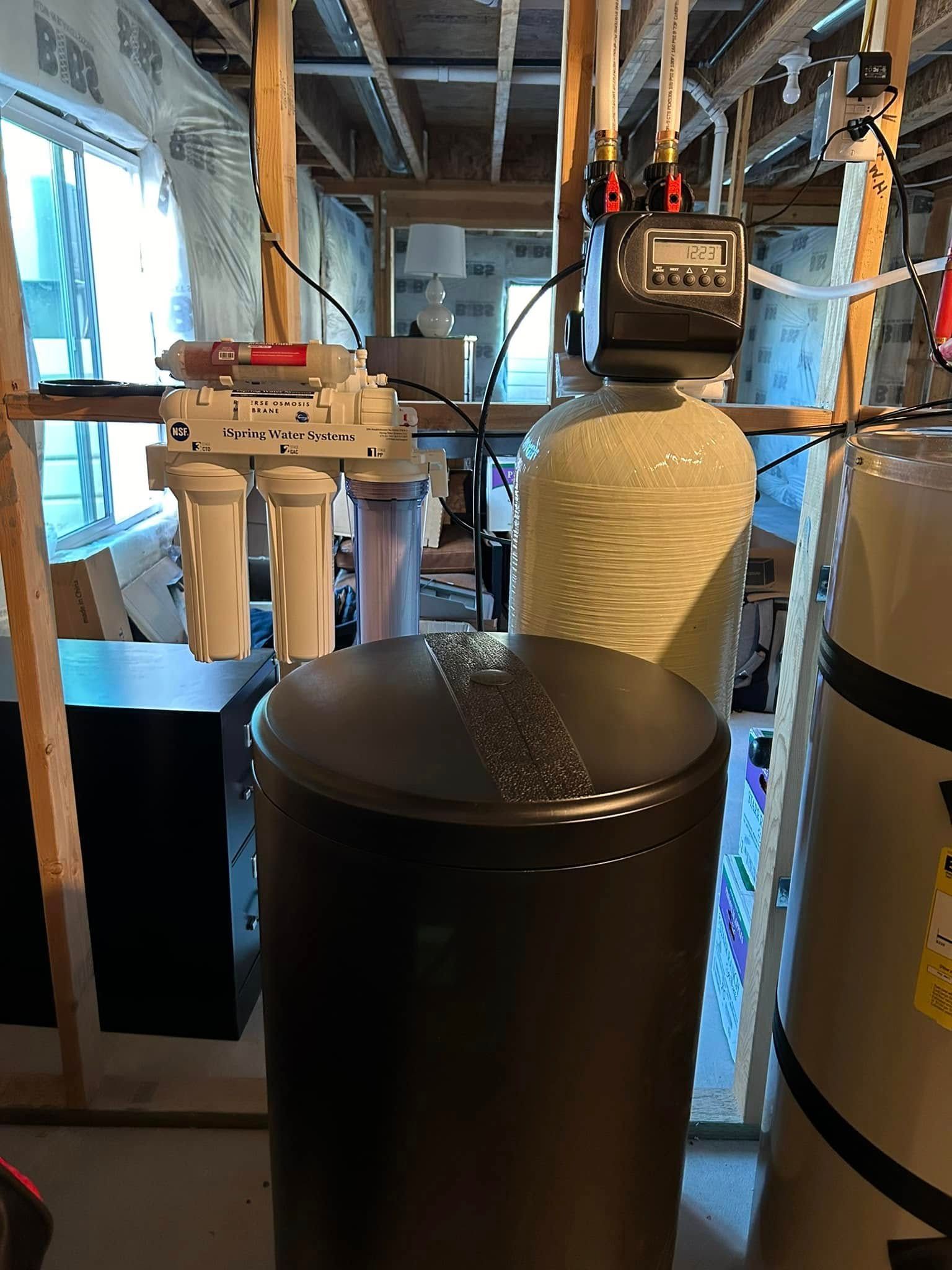 Water filtration system in basement: reverse osmosis, softener, holding tank. Plumbing and wooden supports visible.