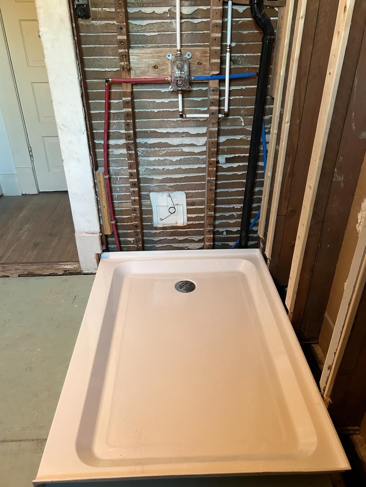 Pink shower pan installed against exposed wall studs with plumbing.