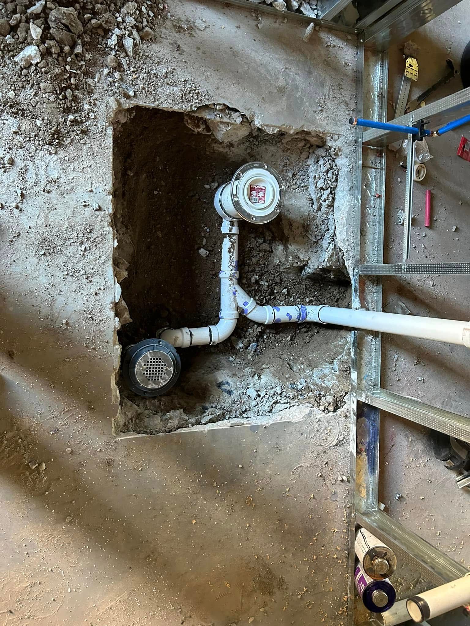 Pipes in a rectangular hole in concrete, with various white PVC fittings and some PEX tubing.