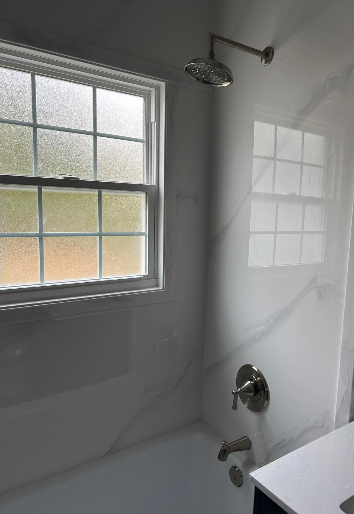 Bathroom with frosted window, shower head, faucet, and white marble-look walls.