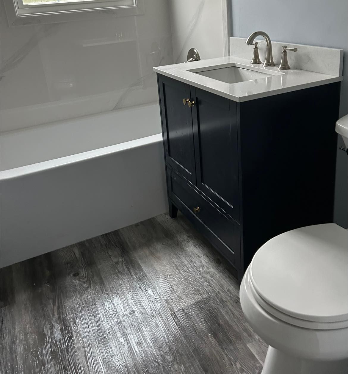 Bathroom with a navy vanity, white countertop, and gray wood-look flooring. A toilet and tub are also visible.