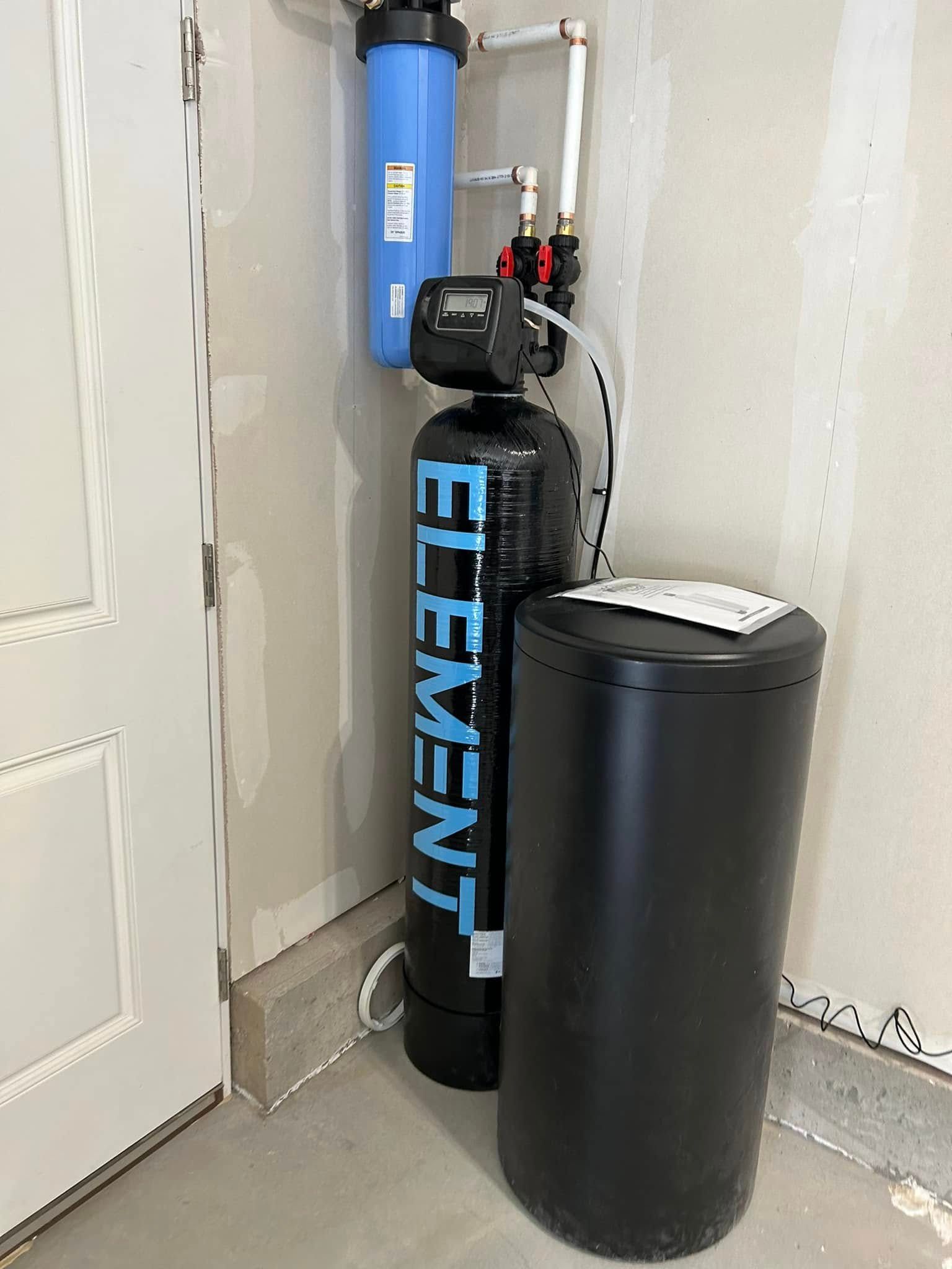A water filtration system in a corner of a garage. Black and blue tanks with white piping.