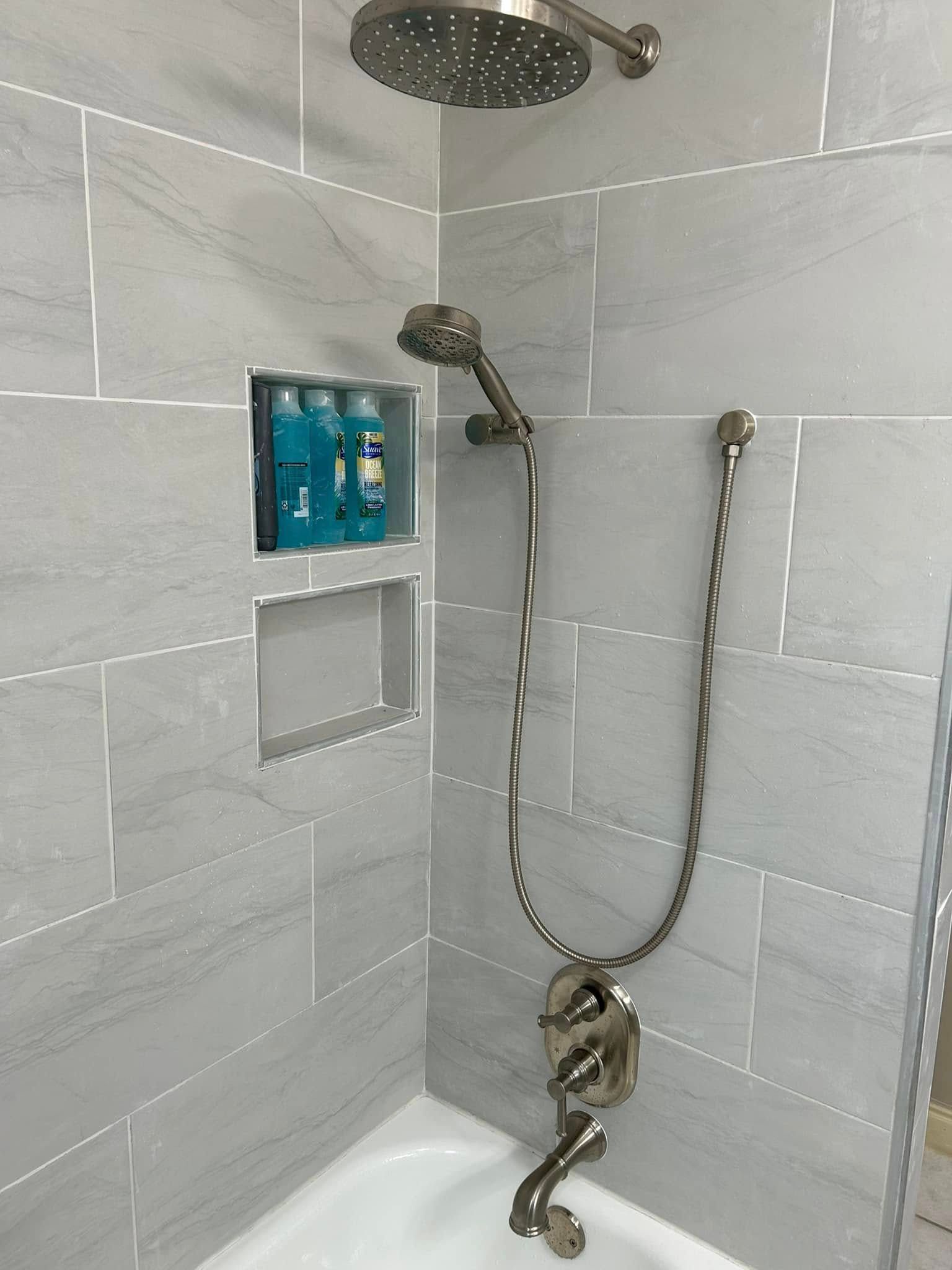 Shower with gray tiled walls, two shower heads, and built-in shelf with toiletries.