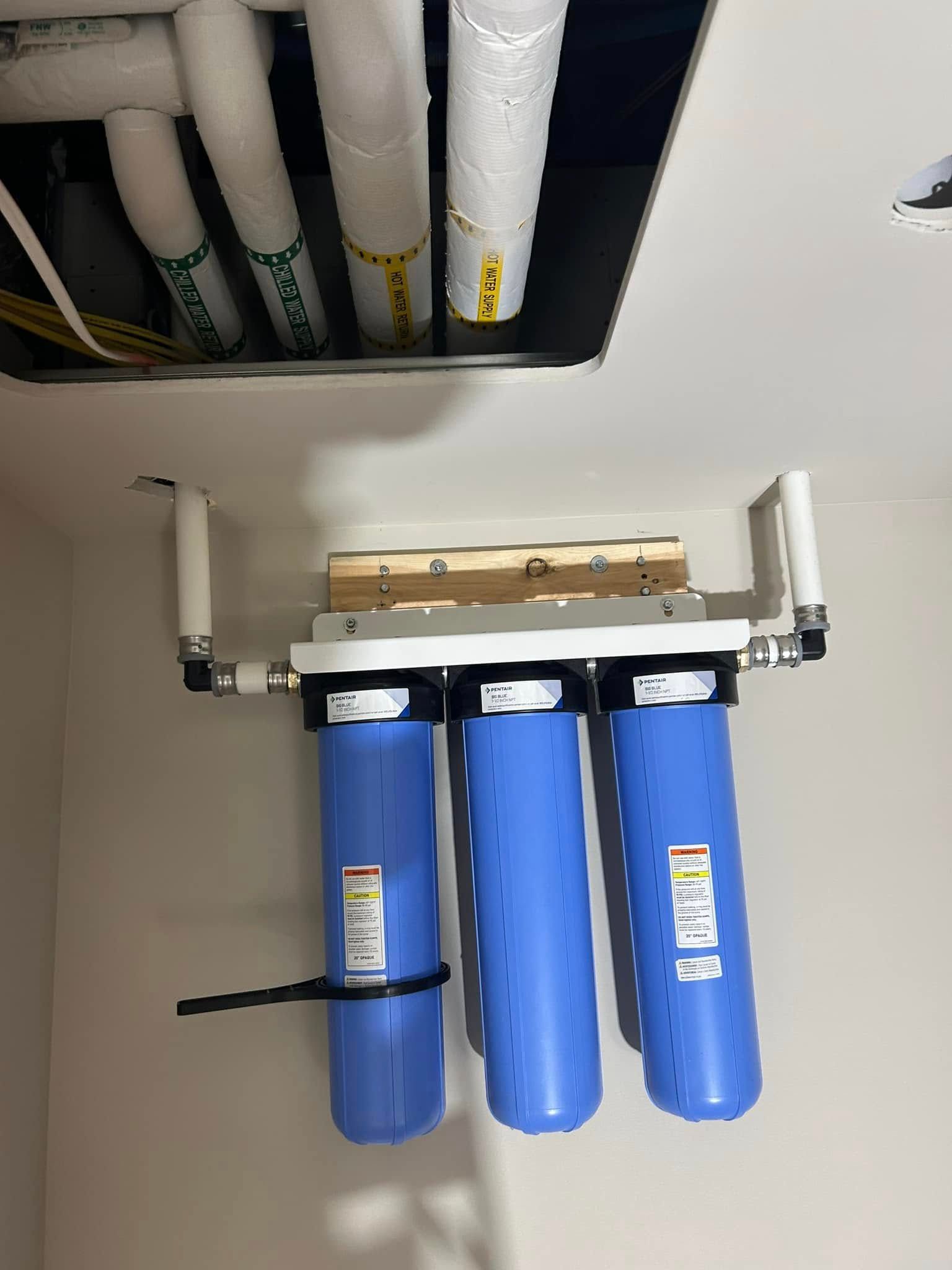 Three blue water filter housings mounted on a white bracket, pipes above.