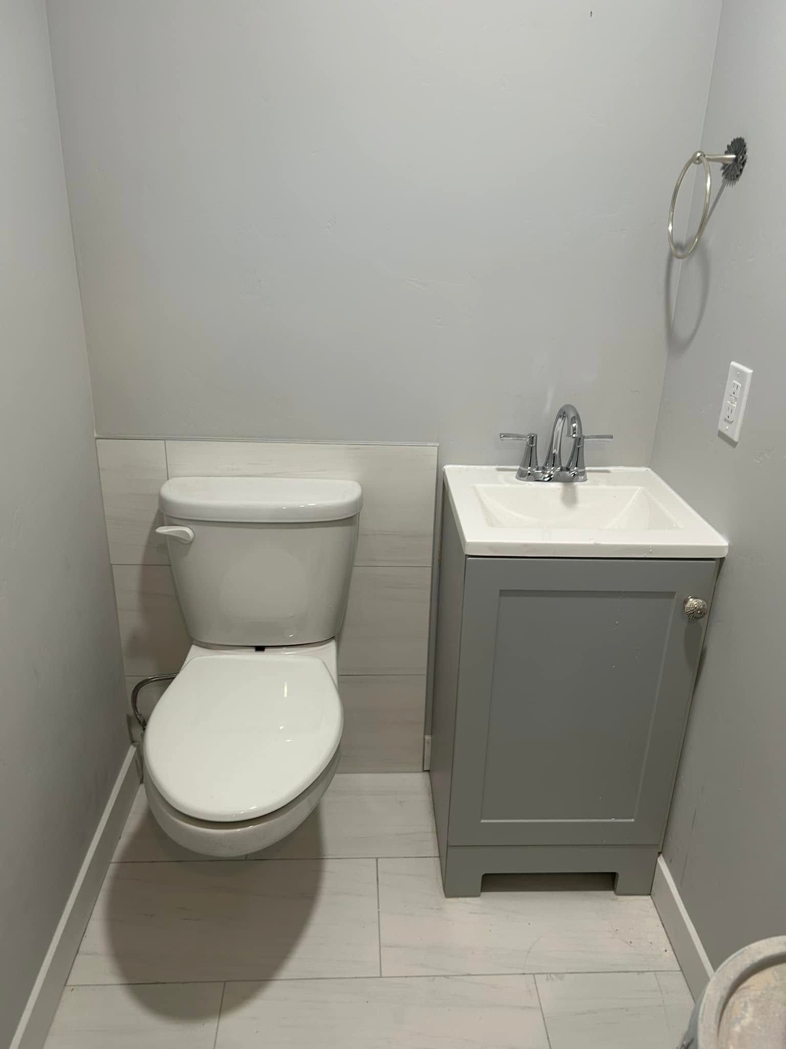 Small gray bathroom with toilet, sink, and cabinet against white-tiled wall and floor.