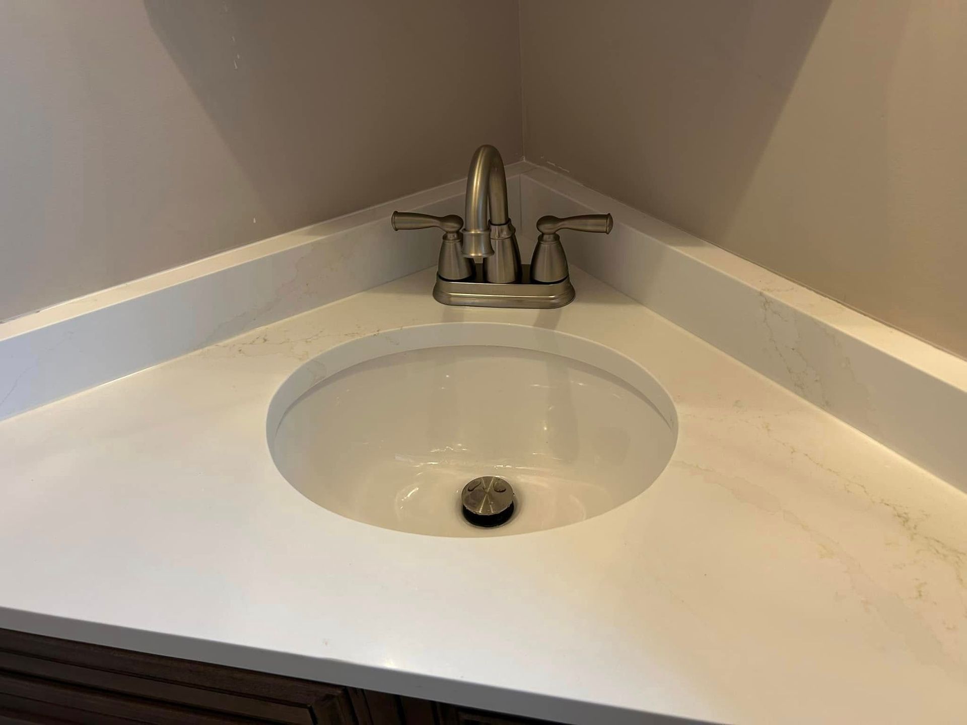 Corner bathroom sink with white countertop and brushed nickel faucet.