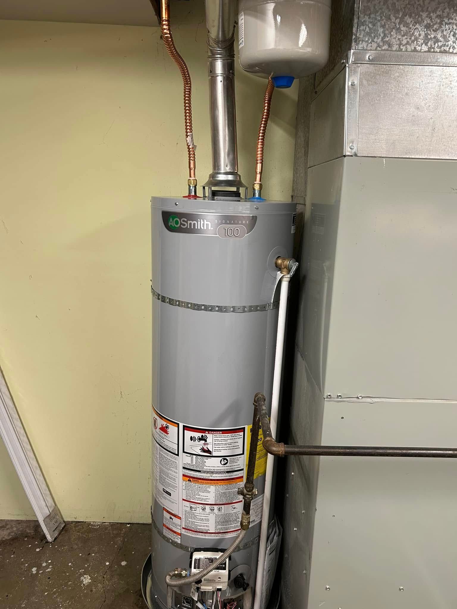A tall, gray water heater with copper pipes in a utility room next to a furnace.