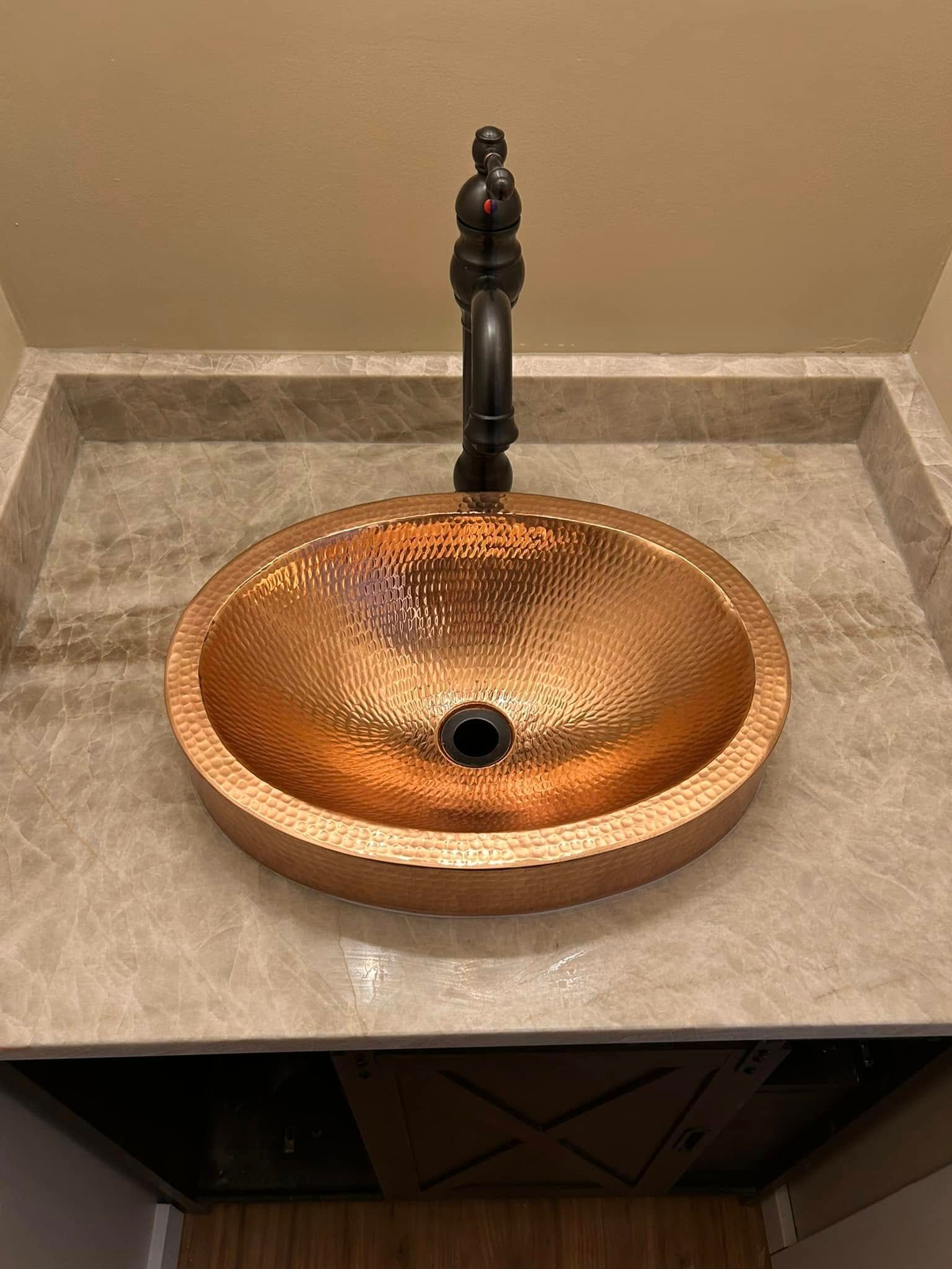 Copper hammered-metal sink with black faucet, set in a light marbled countertop.