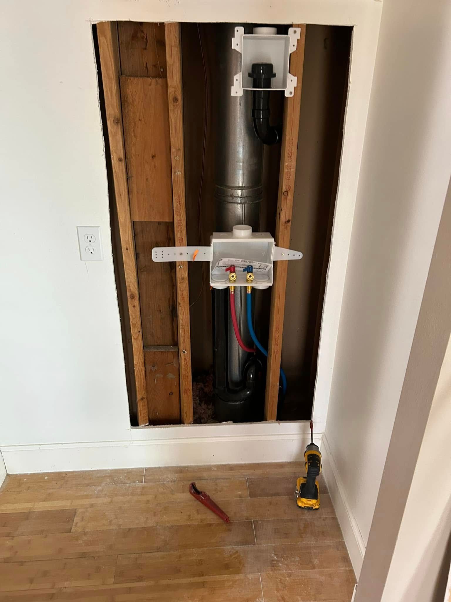 Plumbing rough-in inside wall cavity. Pipes, valves, and electrical outlet visible, alongside studs.