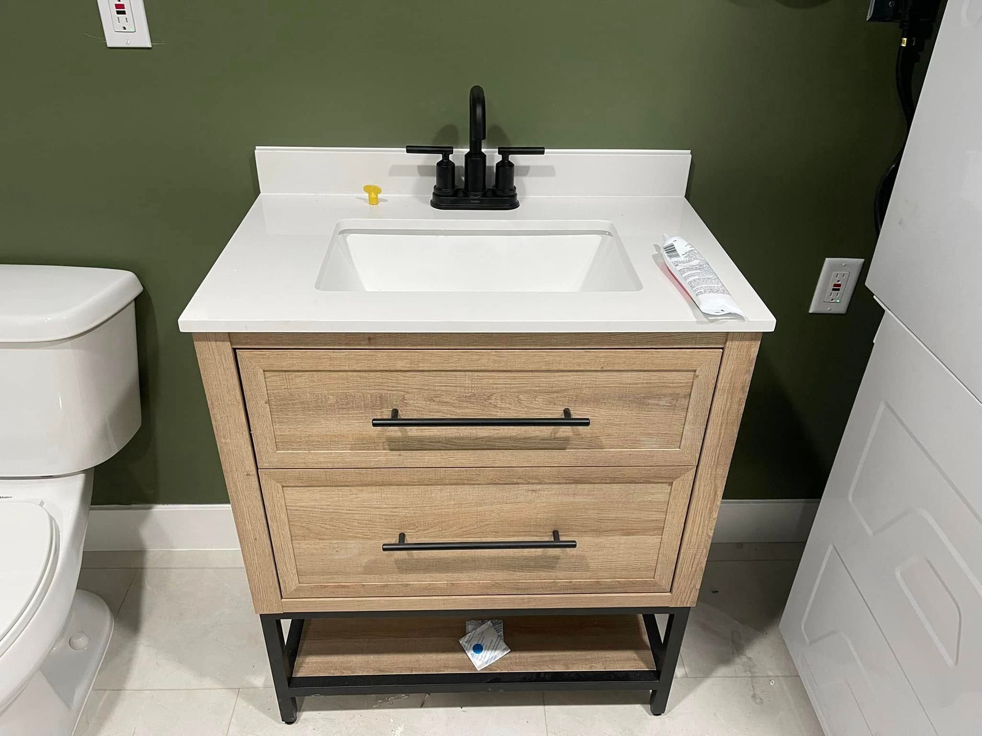 Bathroom vanity with light wood cabinet, white countertop, black faucet, and rectangular sink.