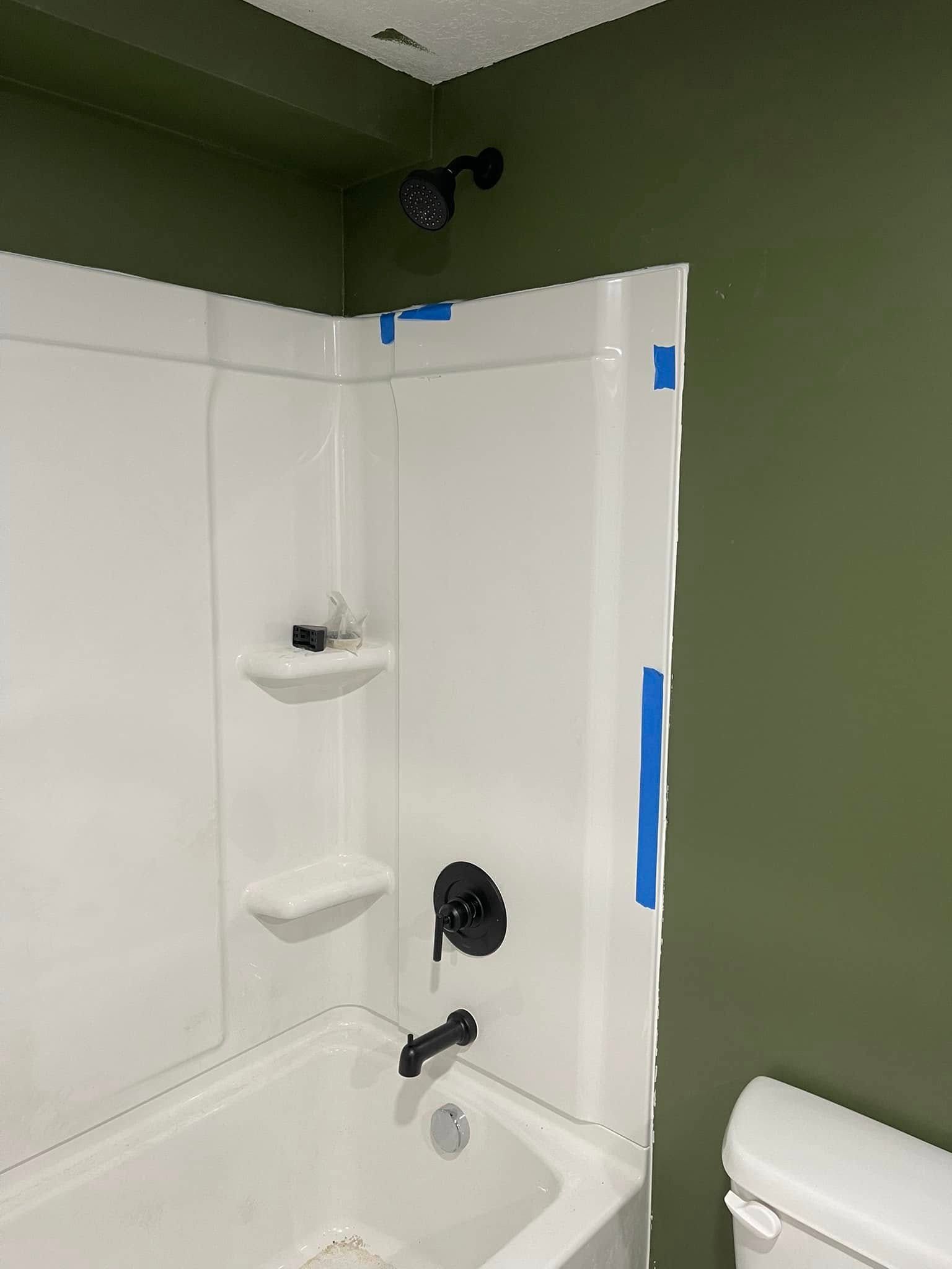 Bathroom with white shower/tub, black fixtures, and green walls.