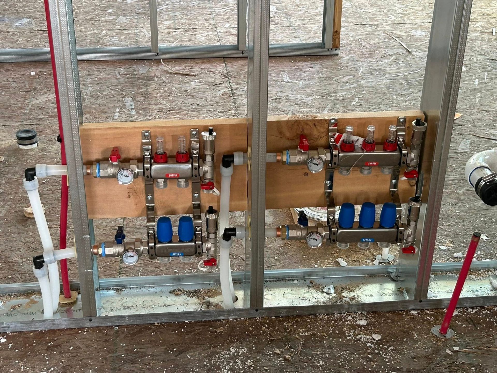 Plumbing manifold system installed on a wooden board within a metal frame construction.