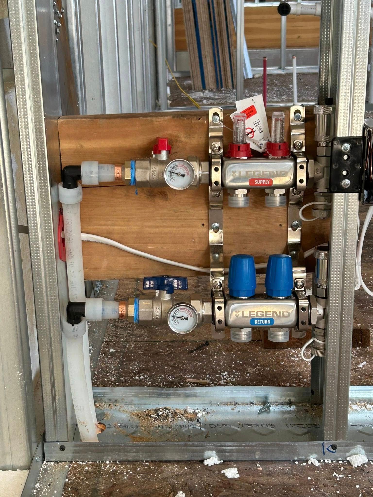 Plumbing system, copper pipes, pressure gauges, control valves, mounted on wood board within a metal frame.