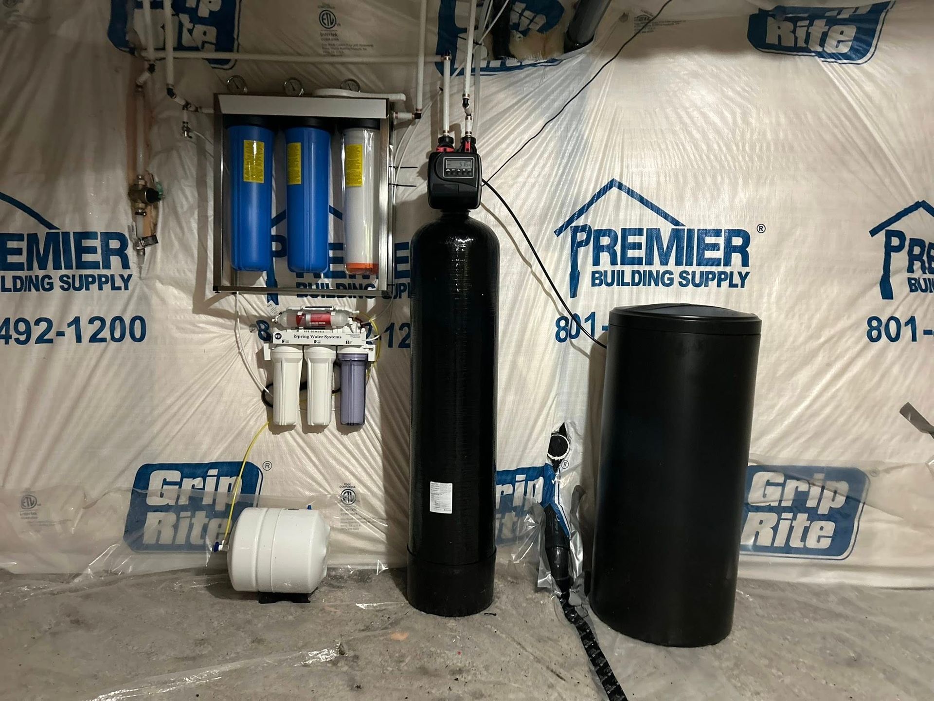 Water filtration system installed in a basement, featuring multiple filter tanks and a storage tank.