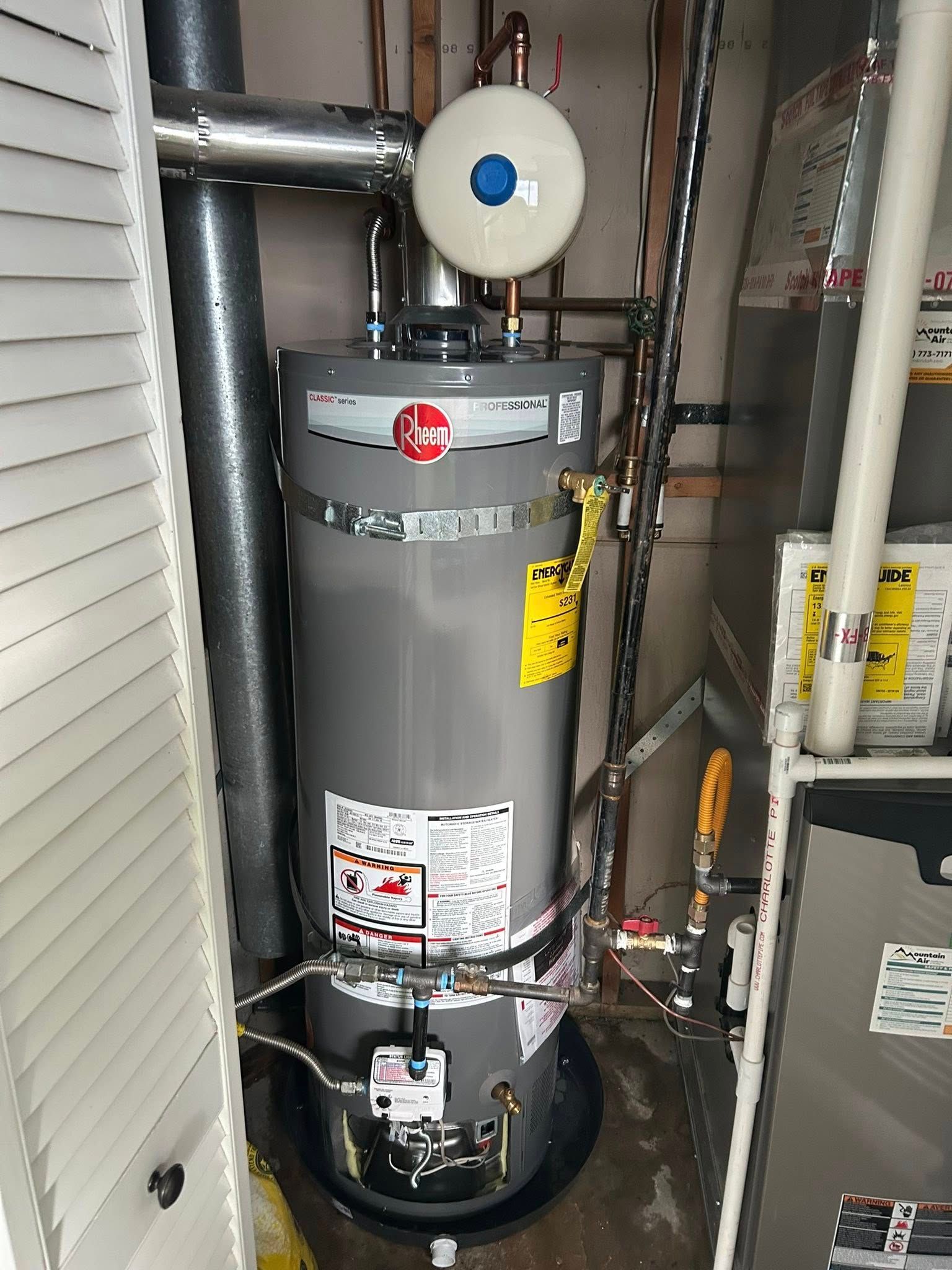 A Rheem water heater in a utility closet with vent pipes, copper tubes, and a furnace.