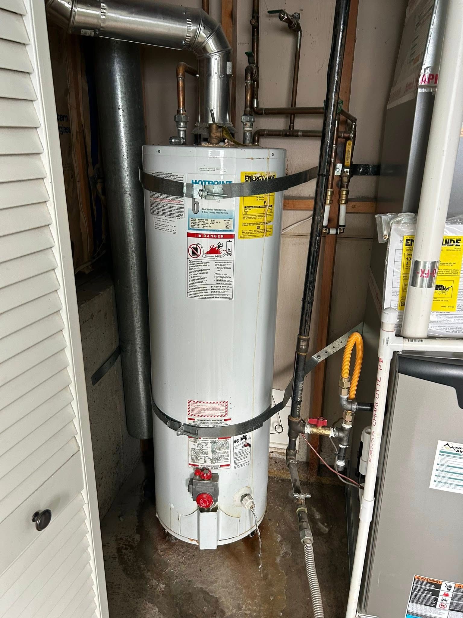 A water heater, pipes, and furnace in a utility closet.