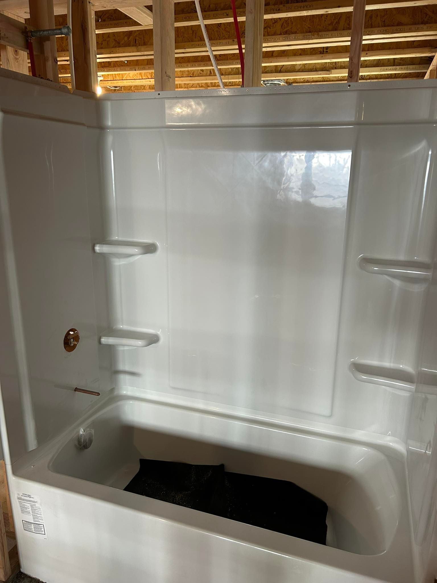 White alcove bathtub with integrated shelves, installed in a partially built bathroom.