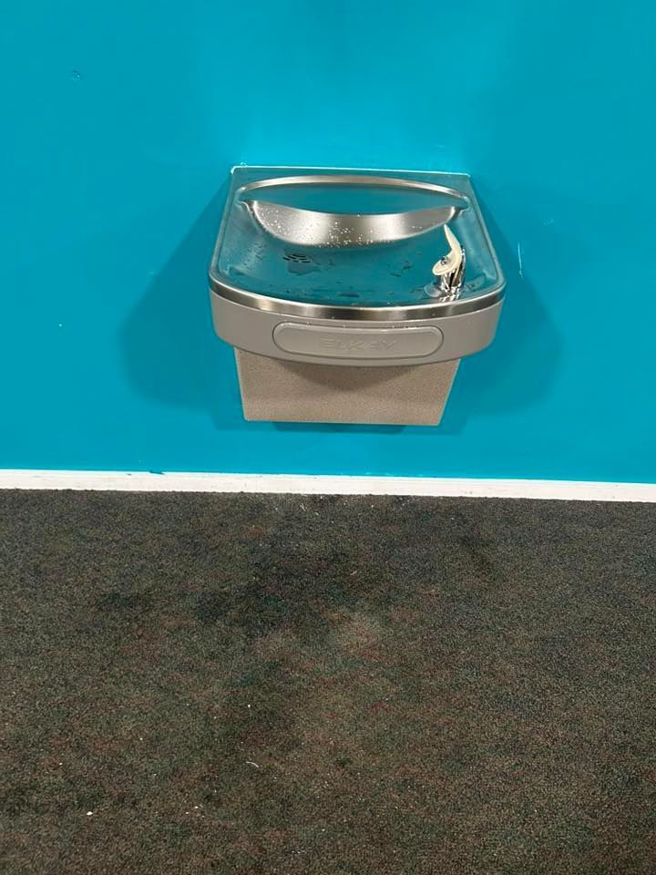 Water fountain on a blue wall above a dark carpet.