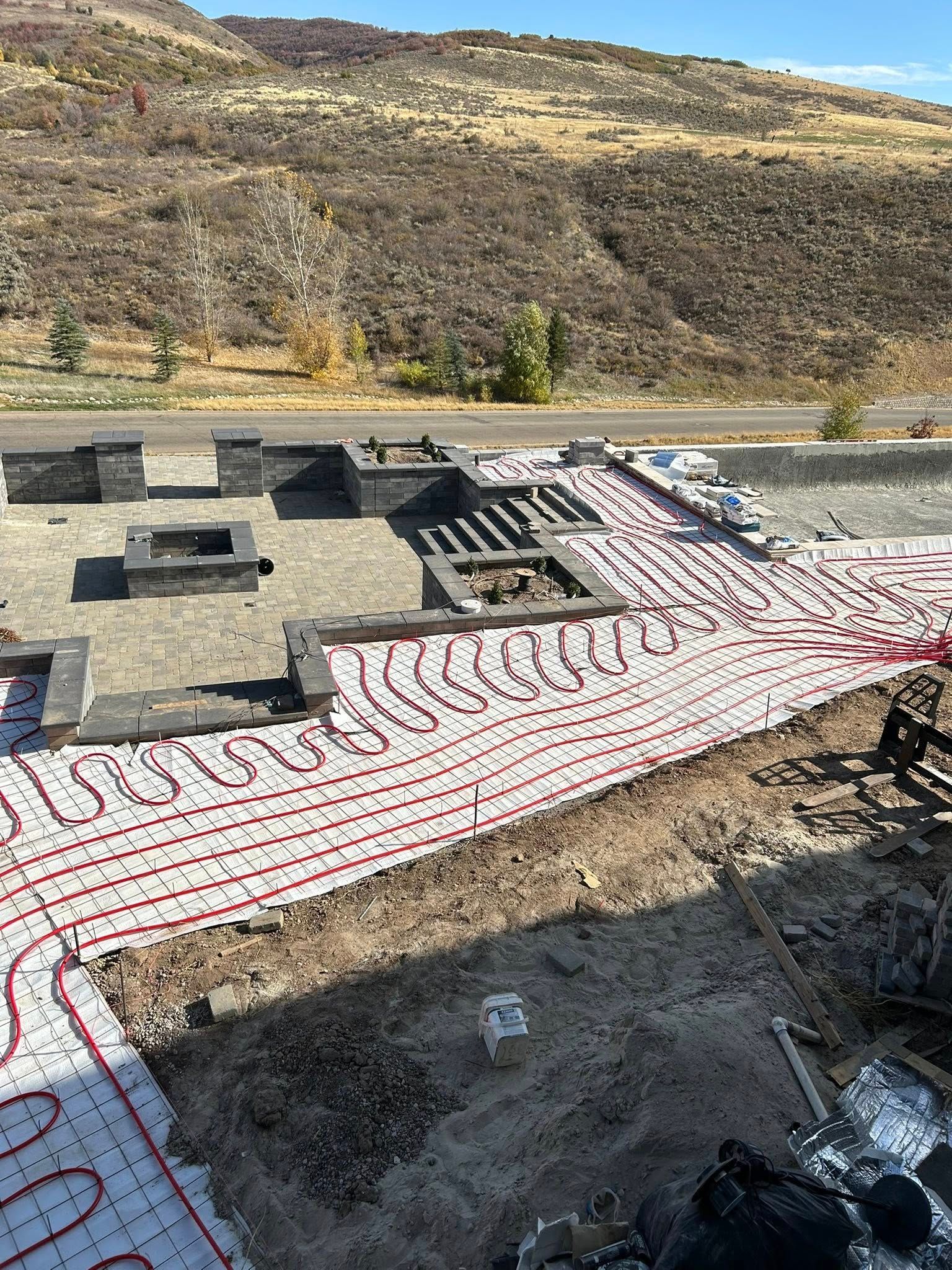 Red pipes laid in patterns, construction site for outdoor area with stone features and hillside.