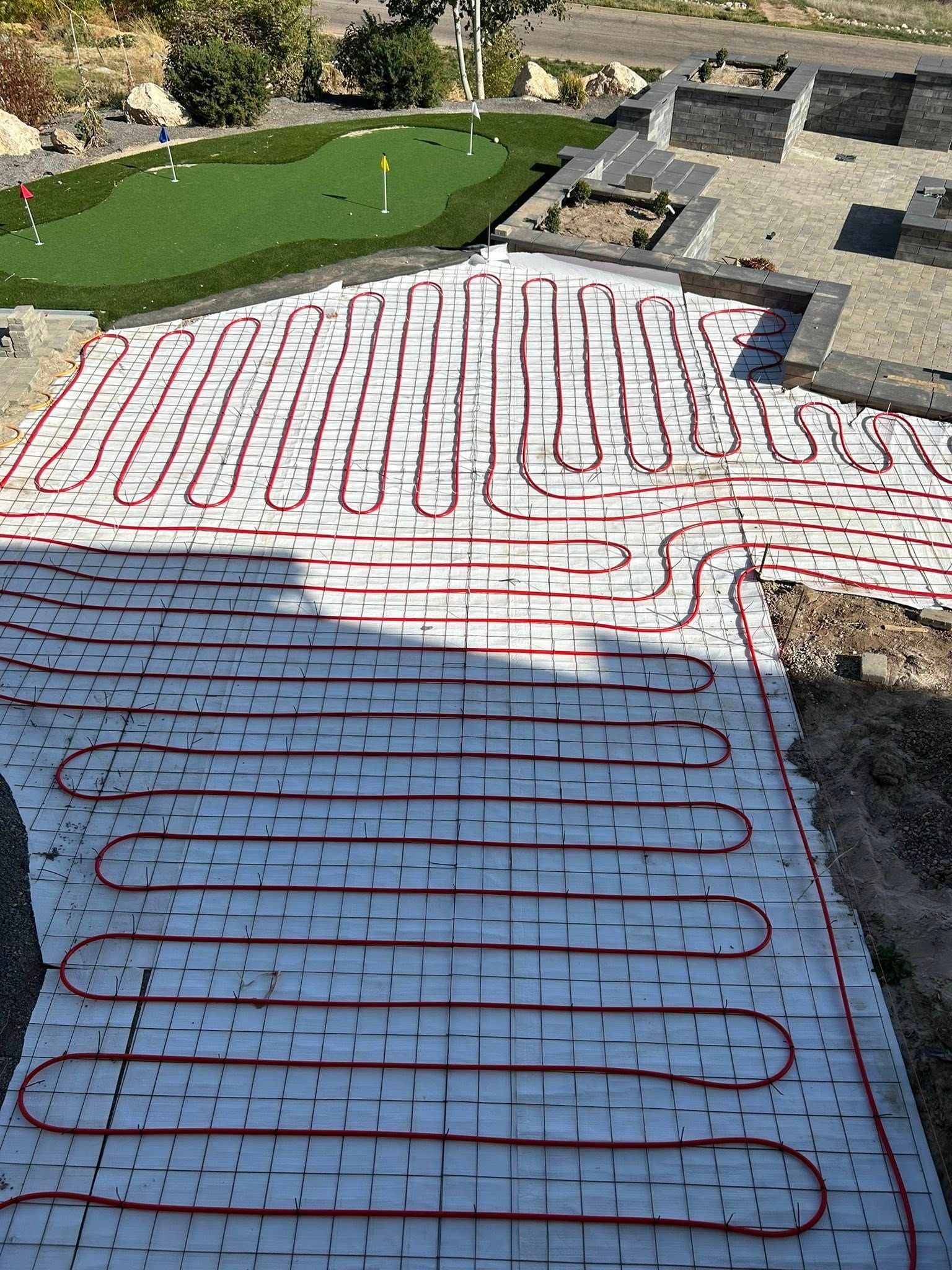 Red radiant heating tubes laid on white sheeting, in a pathway leading to a putting green.