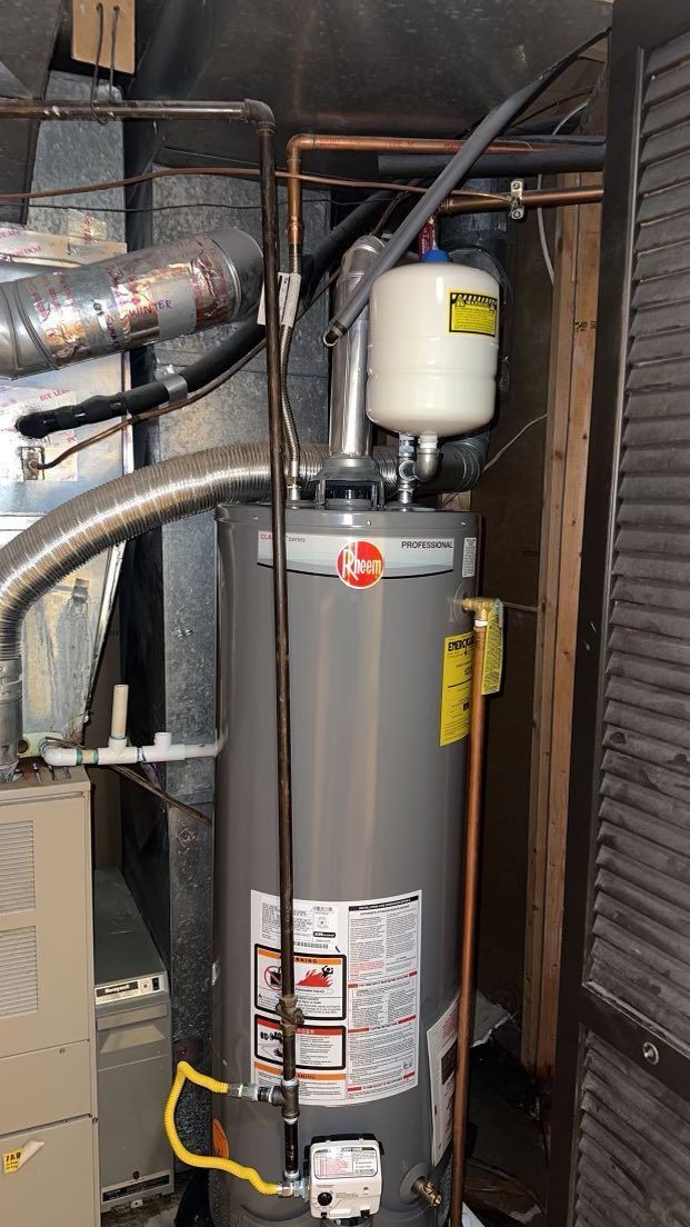 A Rheem water heater in a utility room with attached expansion tank and vent piping.