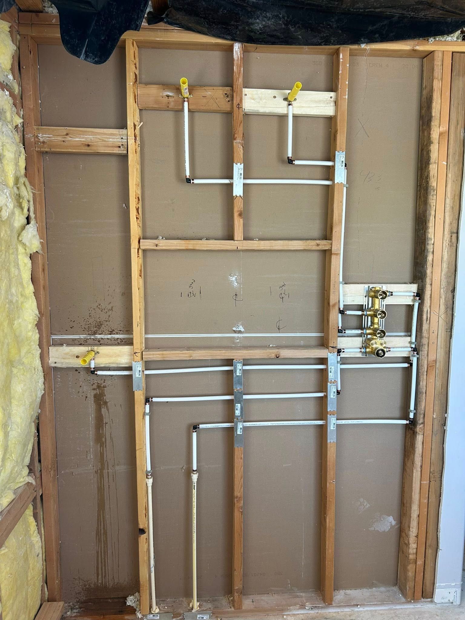 Bare wall with exposed plumbing, including copper pipes and wooden framing, likely for a shower or faucet installation.