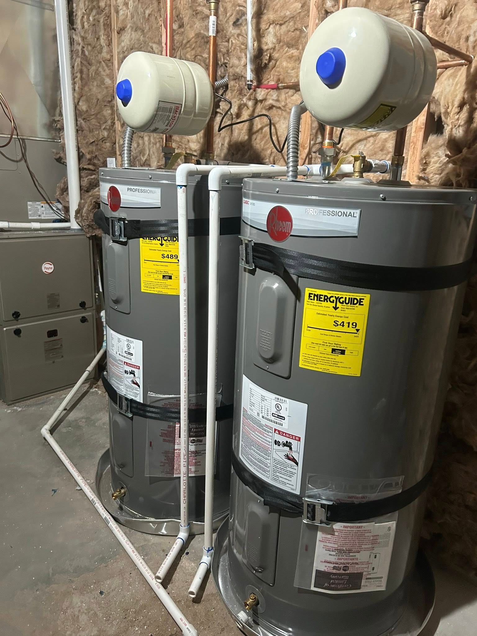 Two water heaters with connected pipes in a utility room.