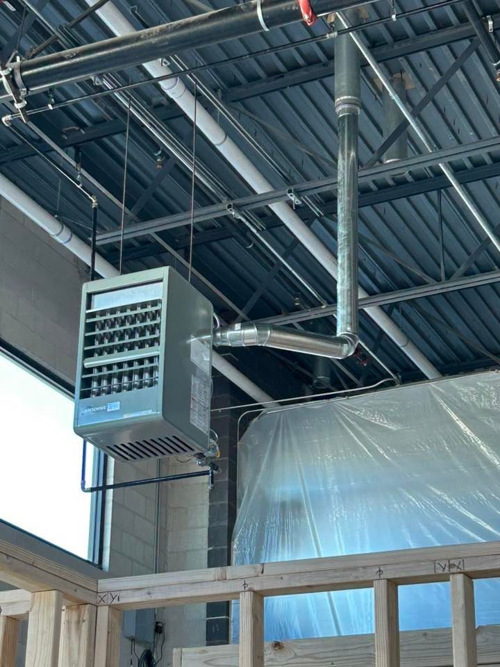 Gray ceiling-mounted industrial heater with metal vent pipe. Construction setting.